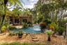 Freeform swimming pool featuring a stone-accented water feature, concrete patio, pebble-style landscaping, and mature palm trees