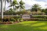 Community entrance monument featuring stacked stone pillars, stucco masonry, and extensive tropical landscaping including manicured lawn and mature pa