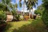 Rear exterior featuring a tile roof, mature palm trees, landscaped garden beds, and expansive lawn area