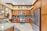 Kitchen featuring stained wood cabinetry, stone countertops, stainless steel appliances, a diamond-pattern tile backsplash, and ceramic tile flooring