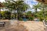 Flagstone patio area featuring a free-form pool with a rock waterfall feature, mature palm trees, and lush tropical landscaping