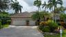Single-story exterior featuring a clay tile roof, two-car garage with arched windows, and a paver stone driveway surrounded by mature palms and profes