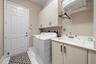 Utility room featuring upper cabinetry, a base cabinet with an integrated basin, a faucet, and white tile flooring