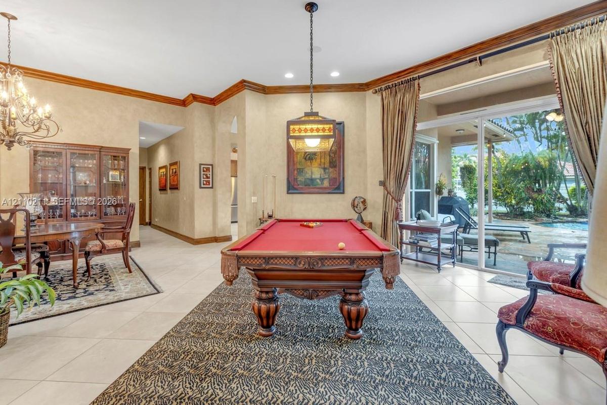 Spacious room featuring neutral tile flooring, crown molding, a decorative multi-light chandelier, a stained-glass style pendant fixture, and large sl