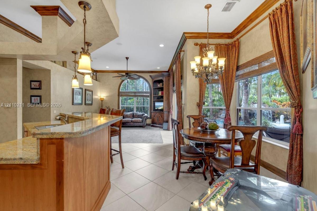 Kitchen featuring stone-finish countertops, natural wood cabinetry, built-in corner shelving, ceramic tile flooring, and decorative multi-light chande