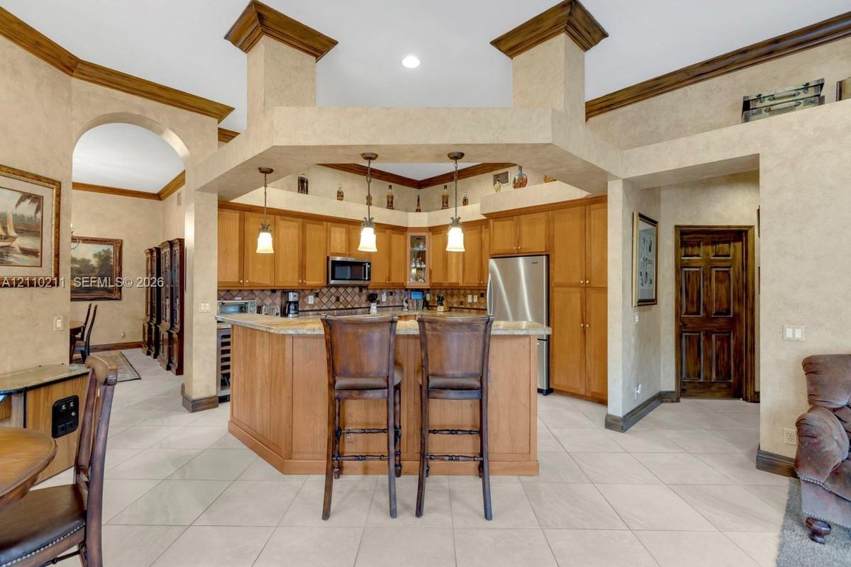 Kitchen featuring custom wood cabinetry, stone countertops, a multi-tiered peninsula island, tile flooring, and hanging pendant lighting