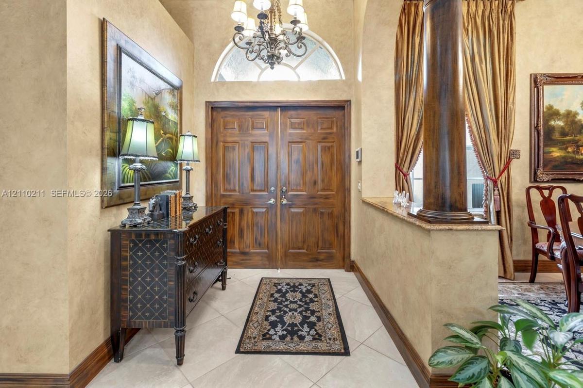 Foyer featuring double wood entry doors, an arched transom window, a decorative chandelier, tile flooring, and a stone-topped half wall with an orname
