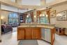 Kitchen island with stone-surface countertop, double-basin stainless steel sink, wood cabinetry, stainless steel dishwasher, and vaulted ceiling