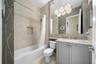 Bathroom featuring a vanity with stone countertop, integrated sink, large wall-mounted mirror, multi-light fixture, and tub with tiled surround and in