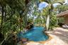 Freeform swimming pool with a stone-accented waterfall, natural stone patio, and mature tropical landscaping