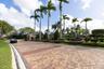 Paver-style roadway featuring a gated stone entrance, mature palm trees, manicured hedges, and professional landscaping