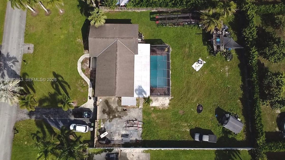 Aerial perspective of a property featuring a screened-in swimming pool, a concrete driveway, a paved walkway, and a perimeter fence