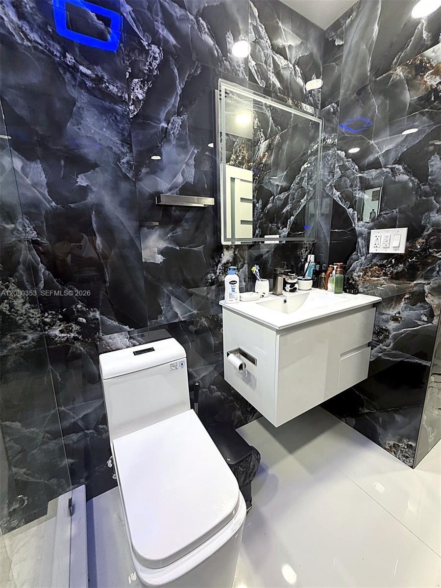 Floor-to-ceiling high-contrast decorative wall tile, white floating vanity, integrated rectangular basin, contemporary low-profile toilet, and rectang
