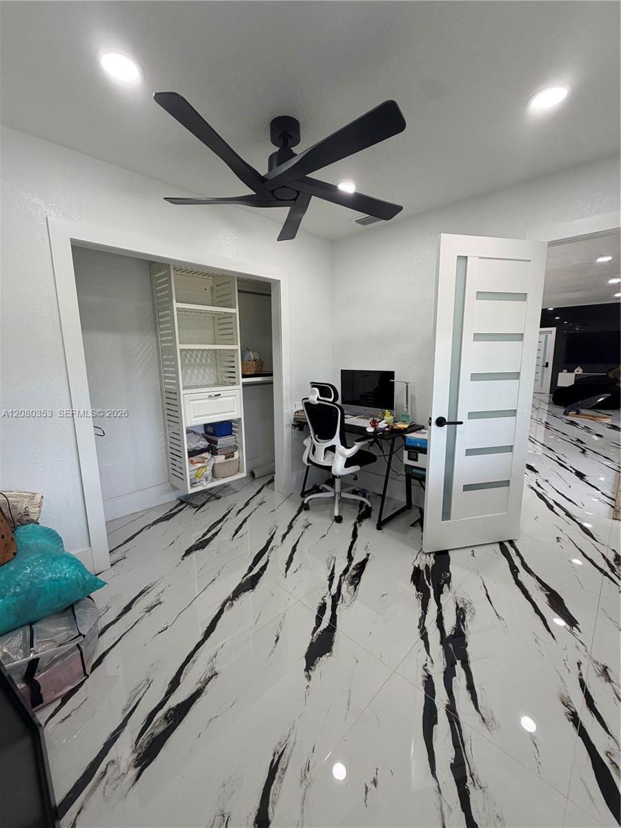 High-contrast polished tile flooring, matte black ceiling fan, white interior door with frosted glass panels, and built-in closet shelving