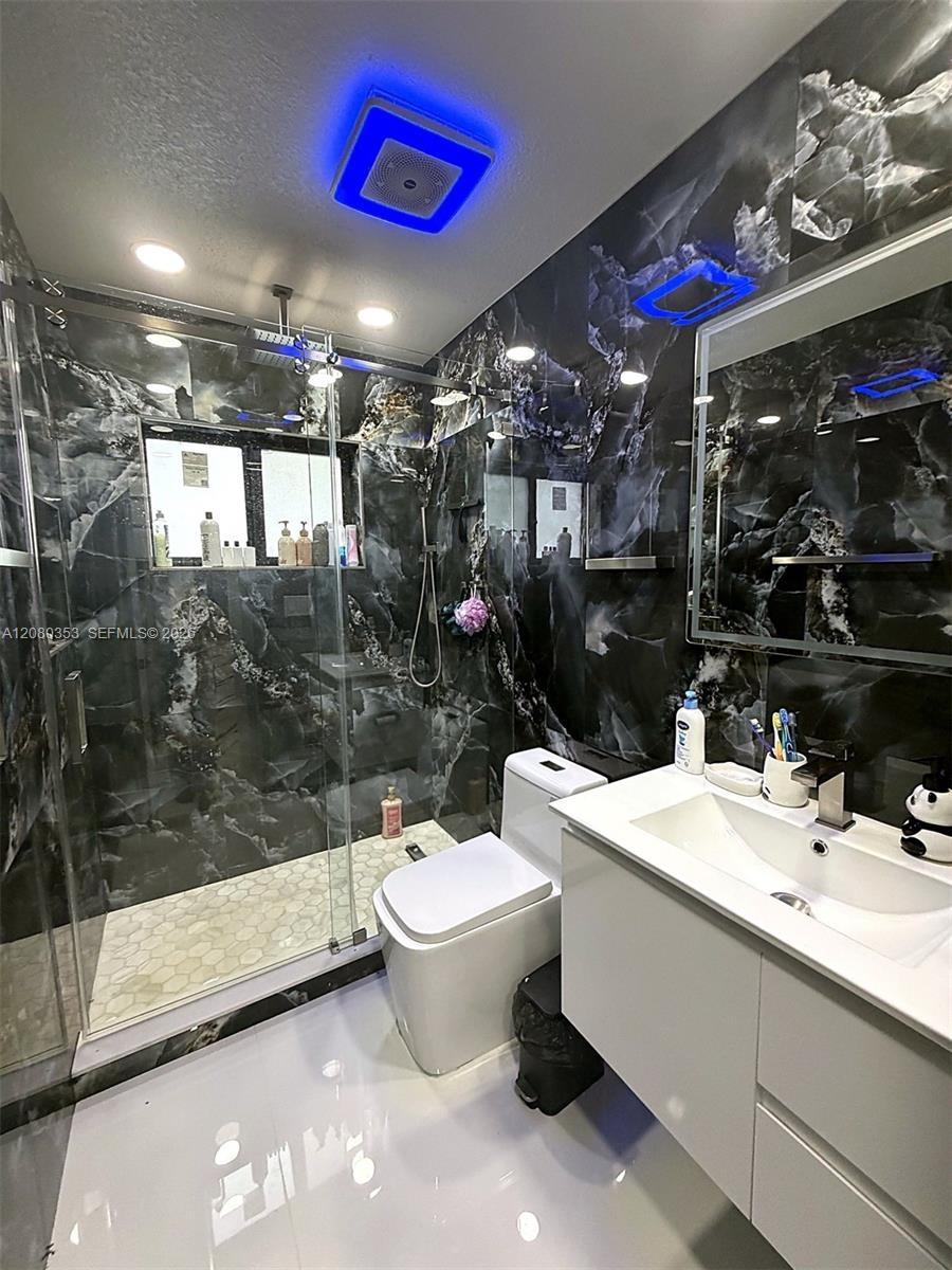 Walk-in shower enclosure with glass panels, full-height dark patterned wall tile, floating vanity with integrated rectangular sink, and recessed ceili