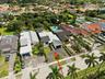 Aerial perspective of a single-story residence featuring a shingled roof, an attached garage, a paved driveway, and established landscaping