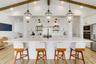 Kitchen featuring a central island with a stone-finish countertop, vaulted ceiling with exposed wood-finish like beams, white cabinetry, lantern-style