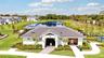Community clubhouse featuring a dark tile roof, exterior lighting fixtures, and a paved walkway, situated on grounds with a retention pond and sport c