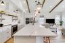 Kitchen featuring a central island with a stone countertop, white shaker cabinetry, stainless steel built-in appliances, decorative ceiling beams, and