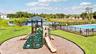 Outdoor recreation area featuring a playground with slides and a climbing wall, a fenced swimming pool, and a water feature surrounded by landscaping.