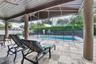 Covered patio with a wood-plank ceiling, structural support columns, and stone tile flooring, featuring an inground swimming pool with a black mesh sa