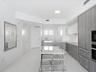 Modern kitchen featuring textured grey cabinetry, white solid-surface countertops, polished white flooring, and built-in stainless steel appliances