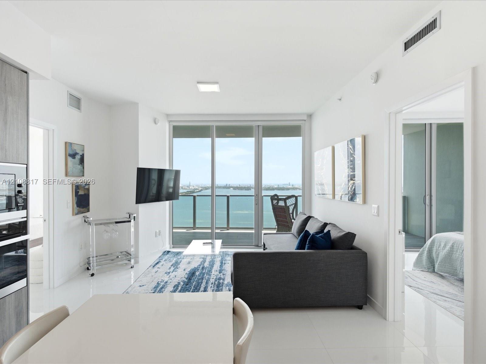 Open-concept interior featuring polished tile flooring, floor-to-ceiling glass doors, and integrated kitchen appliances
