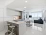 Kitchen featuring two-tone cabinetry, composite countertops, integrated stainless steel appliances, and large-format tile flooring, complete with floo