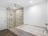 Walk-in glass-enclosed shower with a rainfall showerhead, alongside a built-in soaking tub featuring stone-finish tile surround and wood-finish floori