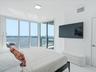 Floor-to-ceiling corner windows, expansive water backdrop, private glass-railed balcony, and recessed ceiling lighting