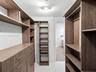 Walk-in closet featuring custom wood-finish cabinetry, floor-to-ceiling shelving, integrated drawer banks, and brushed metal hardware