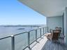 Covered balcony featuring wood-finish flooring and glass-paneled railing with metal framing, overlooking a wide expanse of water