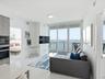 Floor-to-ceiling glass doors, private balcony with water scenery, built-in stainless steel double oven, and polished white tile flooring