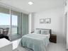 Floor-to-ceiling glass sliding doors opening to a private balcony, water scenery, and polished tile flooring