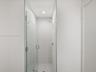 Walk-in shower featuring a frameless glass door, floor-to-ceiling white tile surround, mosaic tile flooring, and a chrome showerhead