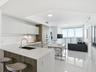 Kitchen featuring matte white cabinetry, wood-finish lower cabinetry, quartz countertops, integrated stainless steel appliances, and large-format tile