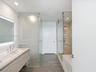 Floating vanity featuring a stone countertop and integrated sink, frameless glass shower enclosure with stone-tile surround, and wood-finish tile floo