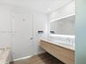 Floating dual-sink vanity with light wood cabinetry, stone-surface countertop, integrated LED mirror lighting, and wood-finish flooring