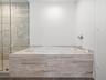 Built-in drop-in bathtub with stone tile surround, glass-enclosed shower, wall-mounted polished chrome faucet, and wood-finish flooring