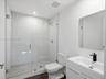 Walk-in shower with a glass enclosure, floor-to-ceiling white tile, modern vanity with a rectangular sink, matte black faucet, and polished mirror