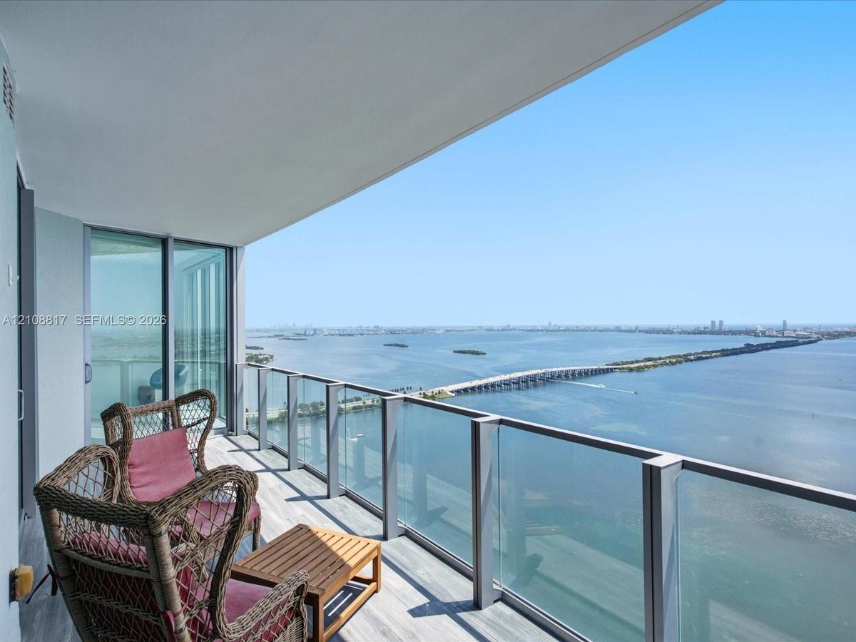 Covered balcony with a glass-panel railing, wood-finish flooring, and full-height sliding glass doors