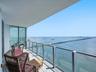 Covered balcony with a glass-panel railing, wood-finish flooring, and full-height sliding glass doors