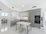 Modern kitchen featuring wood-finish cabinetry, quartz countertops, integrated wall ovens, and high-gloss tile flooring