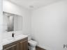 Modern floating vanity with a white rectangular basin, stone-surface countertop, and matte black faucet, featuring wood-finish cabinetry, a large wall