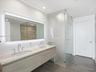 Floating dual-sink vanity featuring stone countertops and polished chrome widespread faucets, complemented by a large back-lit mirror, glass-enclosed 