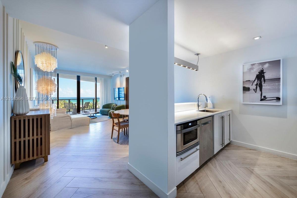 Herringbone wood-finish flooring, white flat-panel cabinetry, integrated stainless steel microwave, quartz countertops, and floor-to-ceiling glass sli