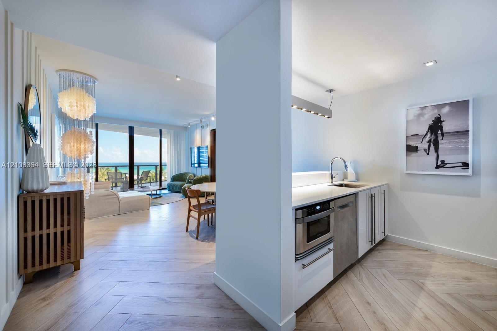 Herringbone wood-finish flooring, white flat-panel cabinetry, integrated stainless steel microwave, quartz countertops, and floor-to-ceiling glass sli