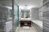 Bathroom featuring floor-to-ceiling stone tile, a soaking tub, a glass-enclosed shower, a floating wood-finish vanity, and recessed lighting
