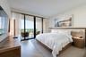 Floor-to-ceiling sliding glass doors, private balcony, wood-finish flooring in a herringbone pattern, and built-in headboard with integrated lighting