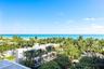 Oceanfront exterior featuring expansive canopy of mature palm trees, multi-level modern architecture, and clear horizon line